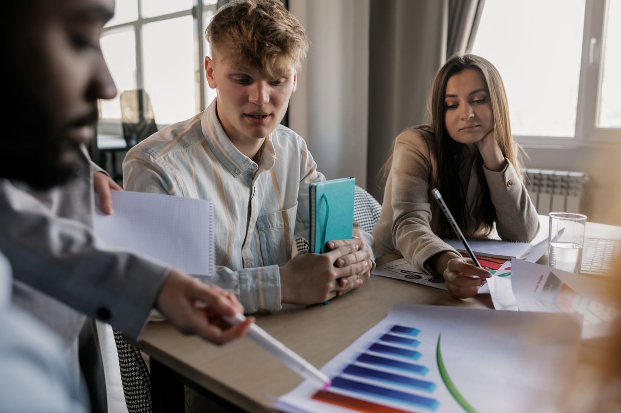 A diverse team of young professionals engaged in a business meeting analyzing graphs and data.